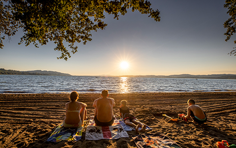 Eine Familie sitzt bei Sonnenuntergang am Seeufer.