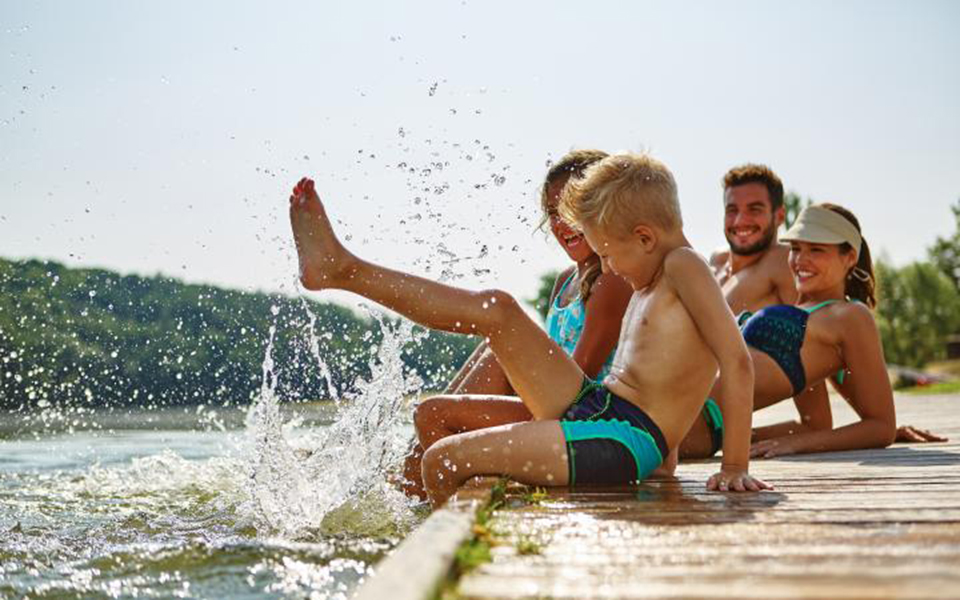 Eine Familie sitzt auf einem Steg und hält die Füsse ins Wasser.