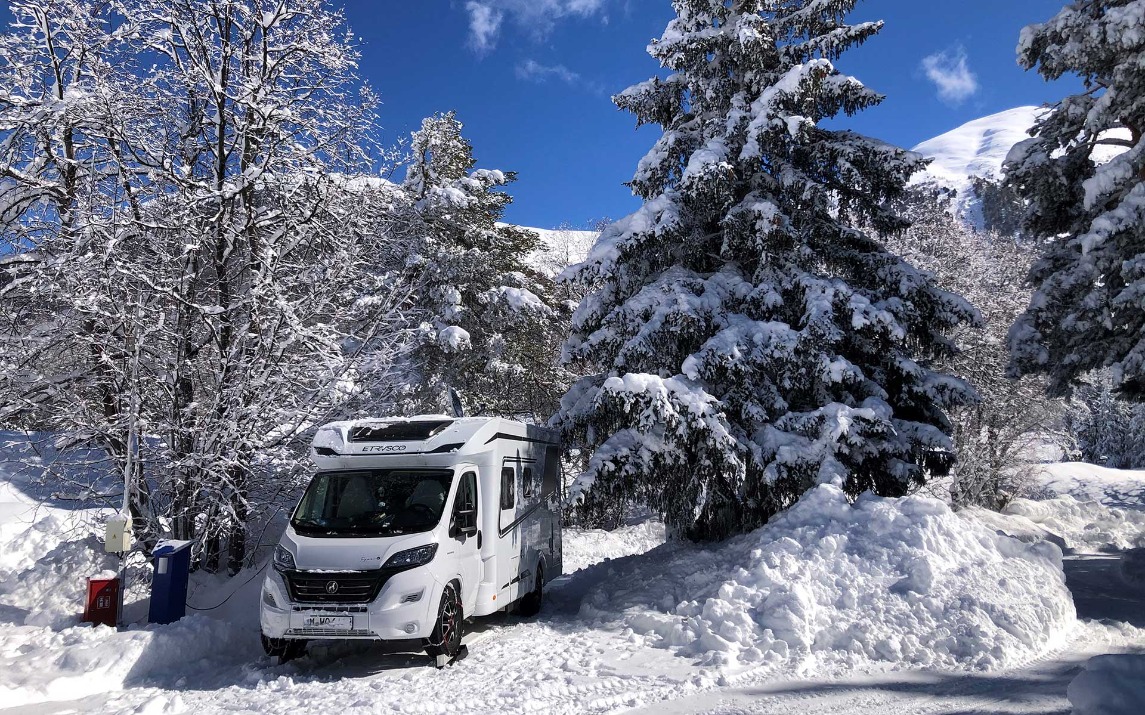 Ein Camper auf einem verschneiten Stellplatz, umgeben von Bäumen.