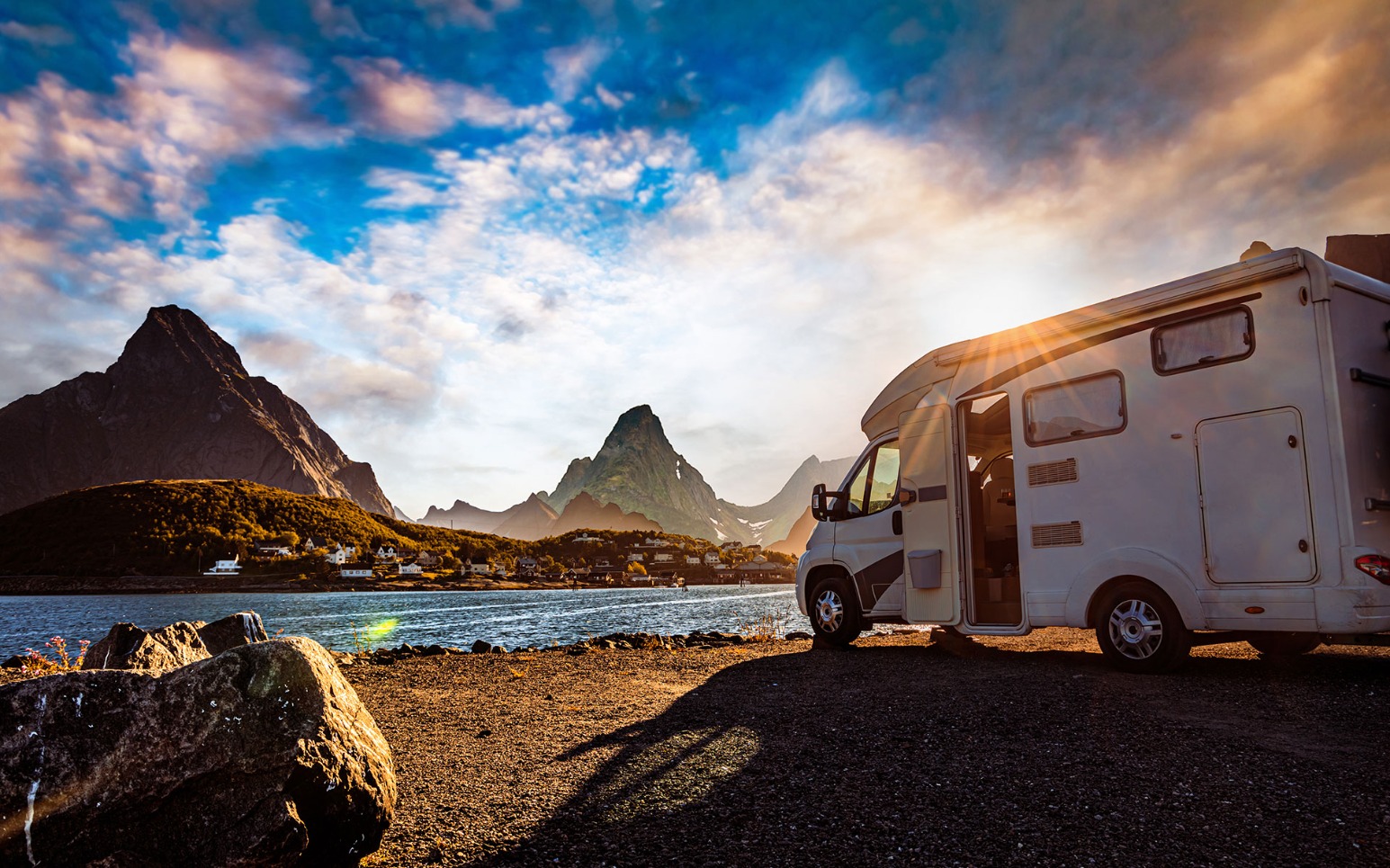 Un camping-car avec la porte ouverte est garé au bord d'un plan d'eau.